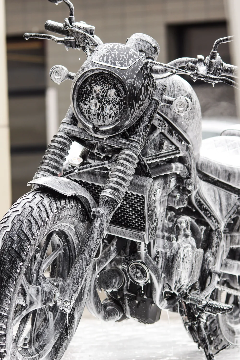 A motorcycle headlight, forks and front wheel covered in wash foam. Illustrative photo.