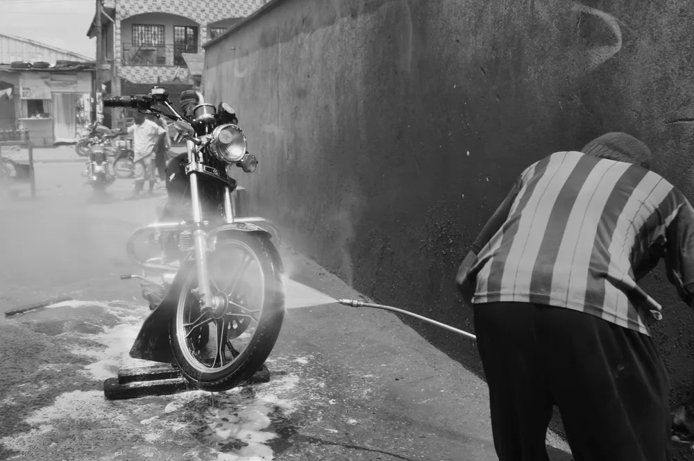 A worker pressure-washes a motorcycle outdoors. Illustrative photo.