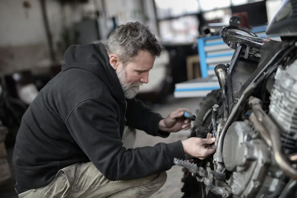A mechanic uses a hand tool beside an exposed motorcycle engine. Illustrative photo.